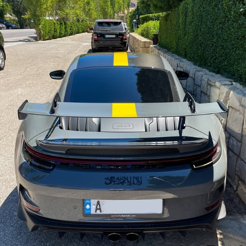 Gray car with a yellow stripe on a street having shahada emblem on the rear