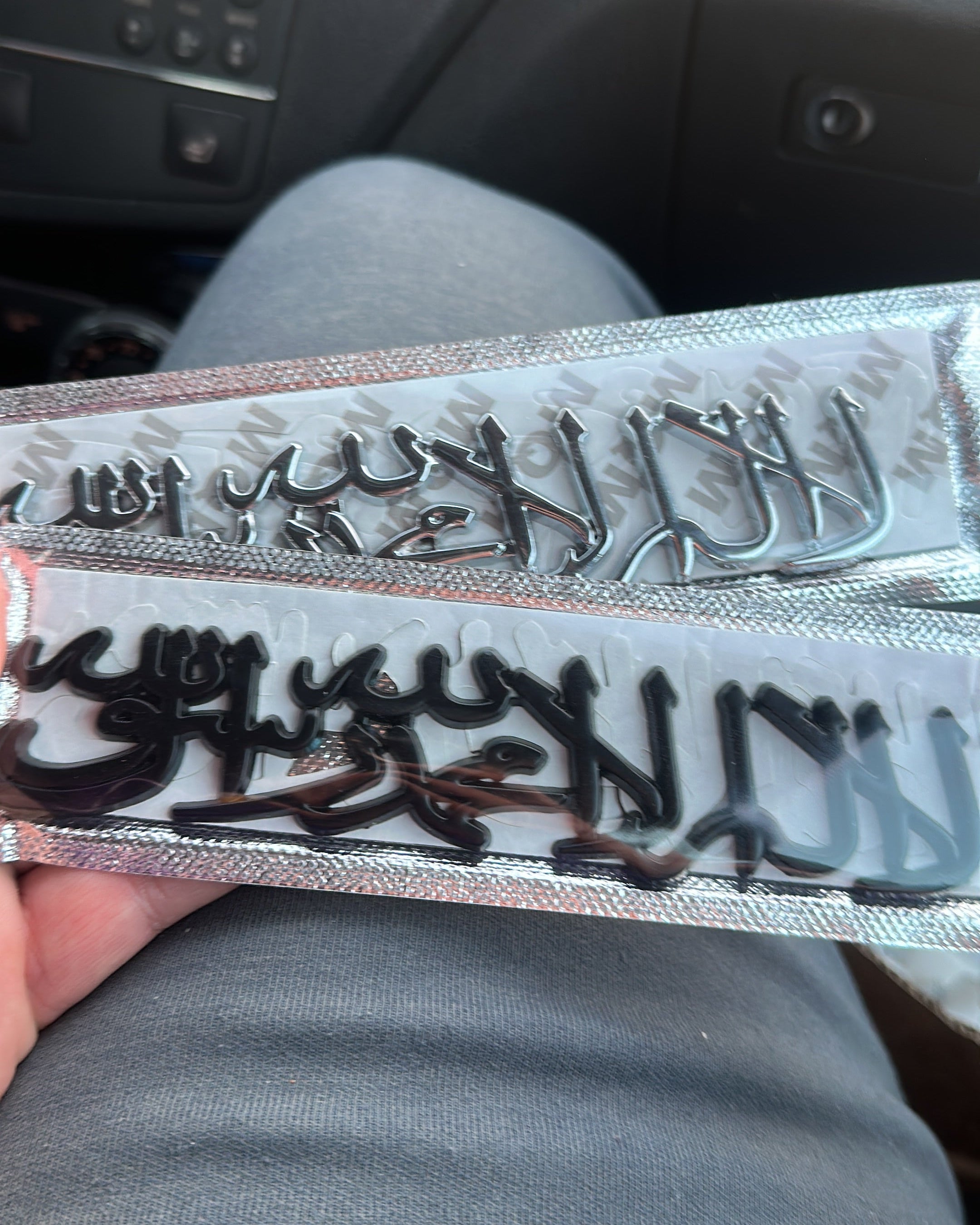 Two metal shahada emblem held by a person inside a vehicle.