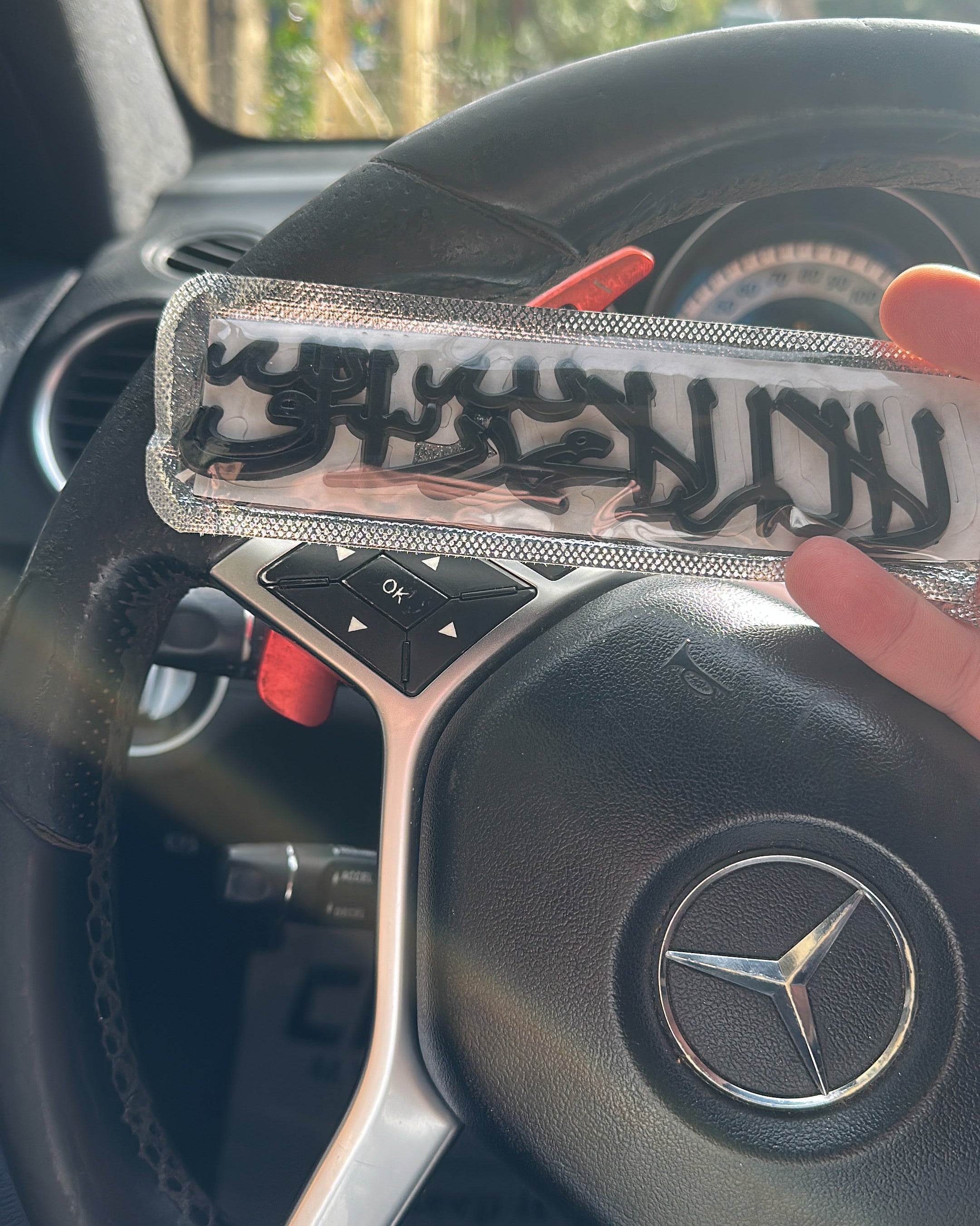 Steering wheel of a Mercedes-Benz car with a hand holding a shahada emblem from qadar btrand