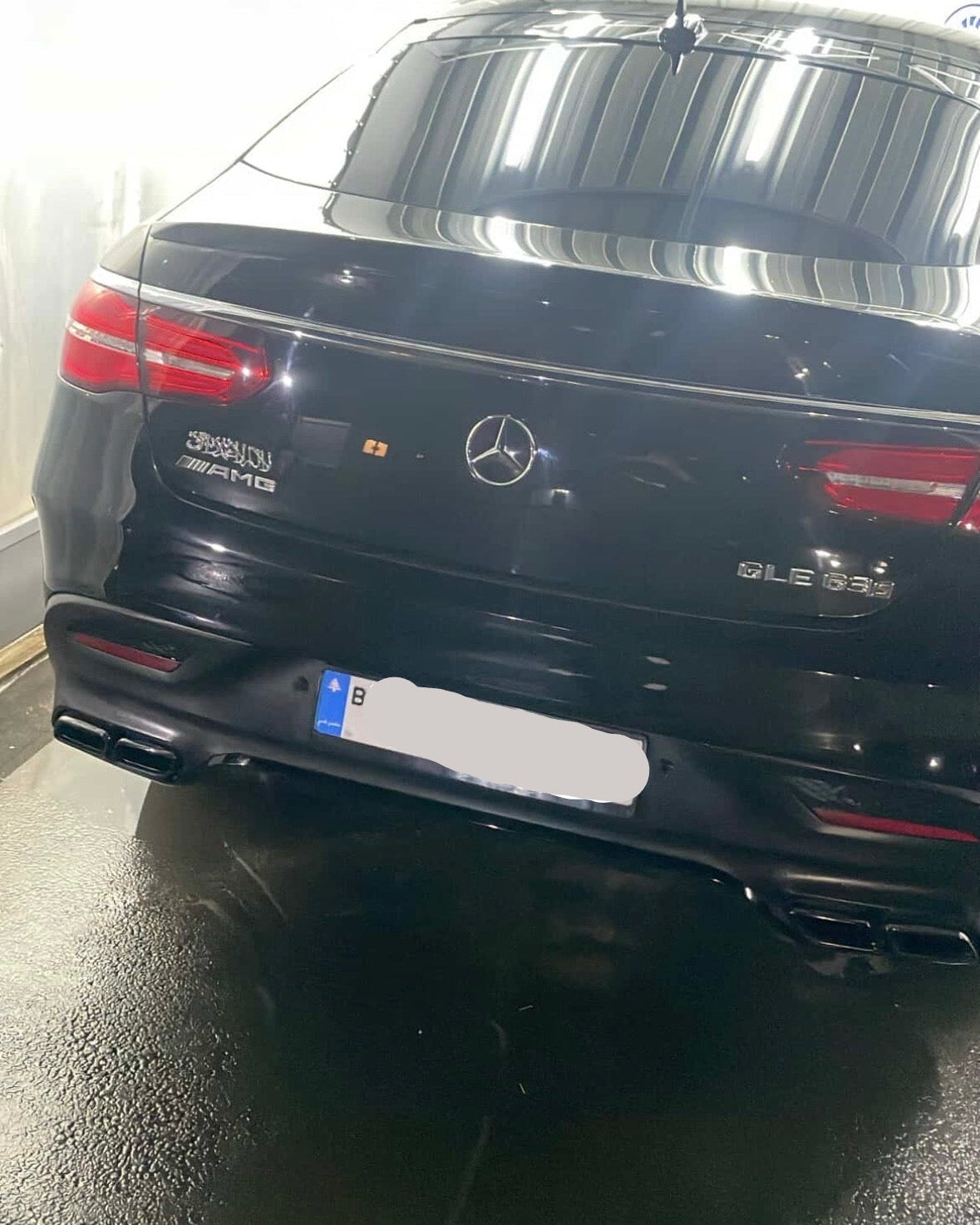 Back view of a black Mercedes-Benz car in a garage with shahada emblem on it